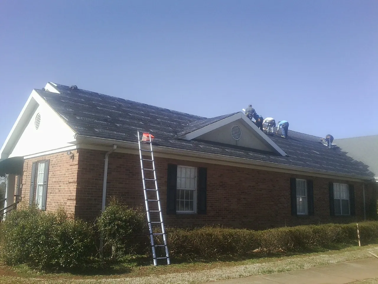 Crew tearing shingles off a brick ranch roof with a ladder set — Metal Roof Repair work by our crew in Nottawa