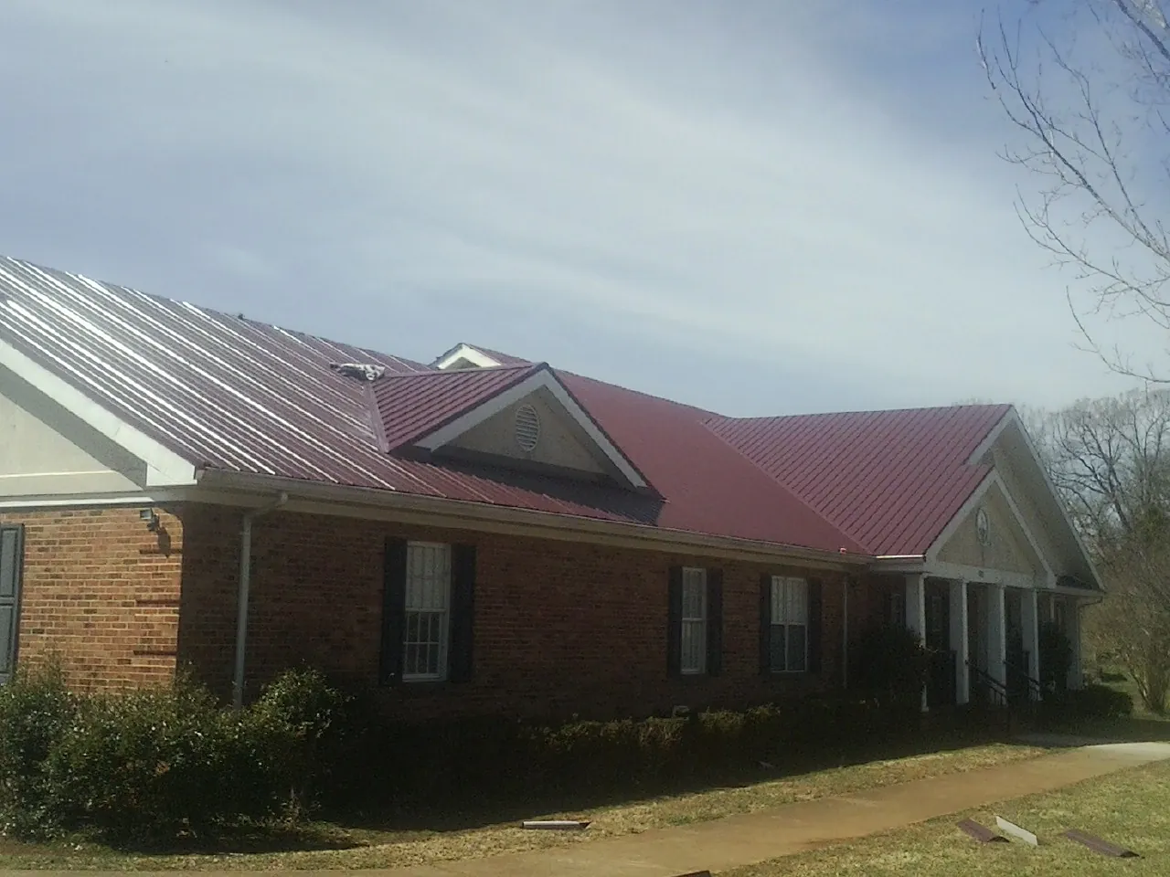 Red metal roof with gabled entries on a long brick building, from a Hail Damage Roof Repair job in Nottawa