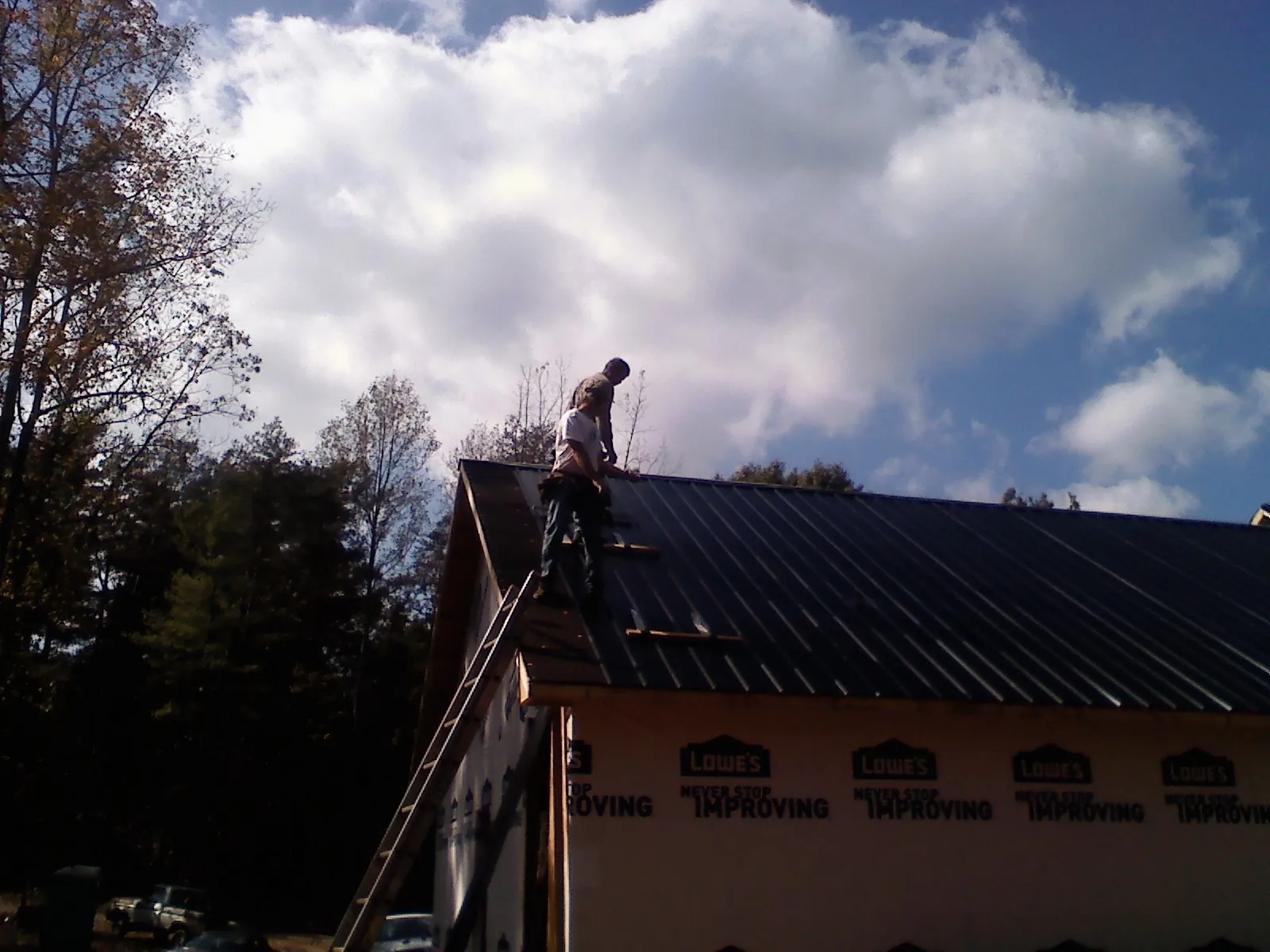 Roofer fastening dark metal panels high against a cloudy sky, from a Roof Inspection job in Nottawa