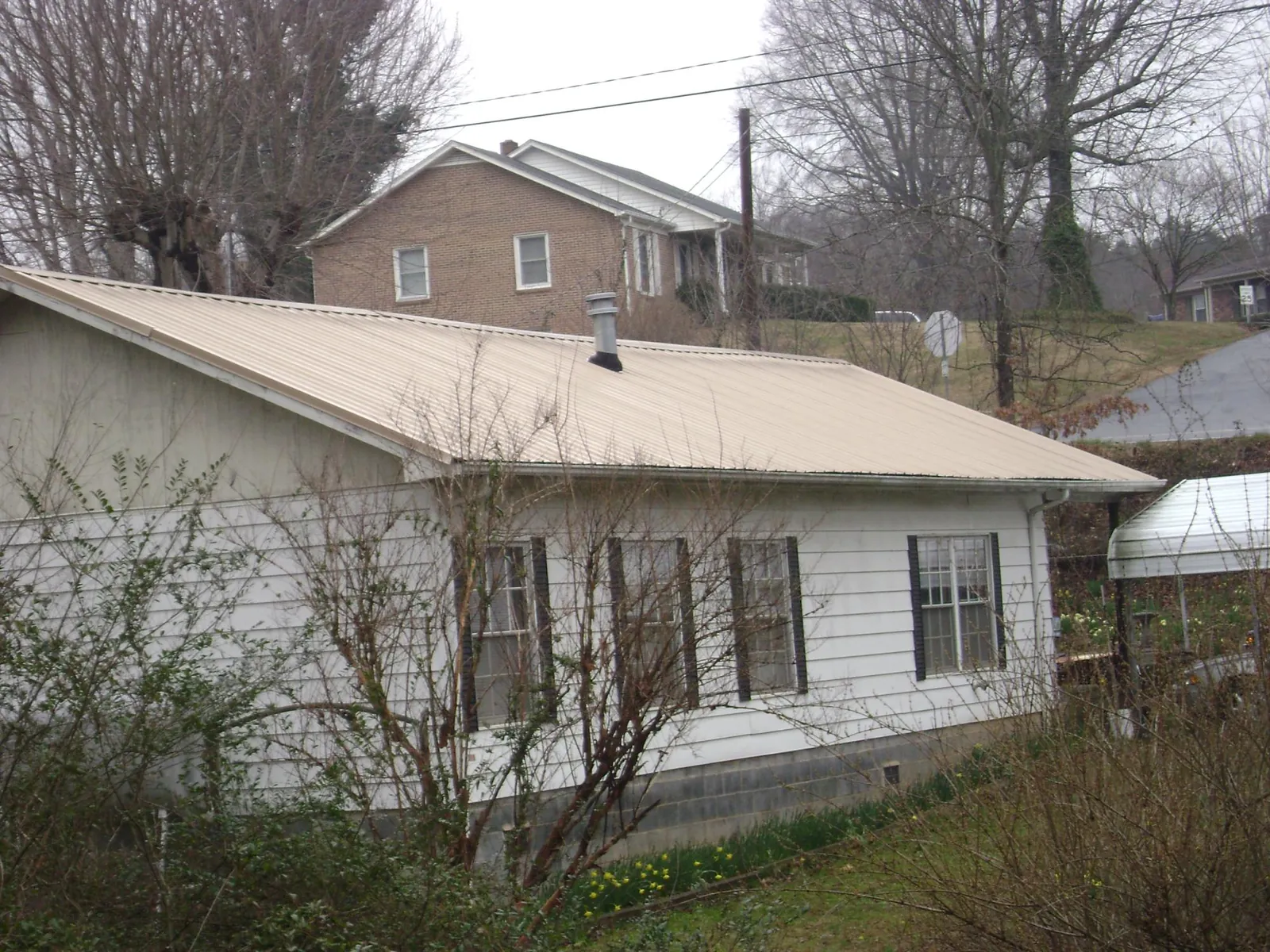 Tan metal roof on a white sided house set into a hillside — Commercial Roofing by Roofing Brothers in Nottawa