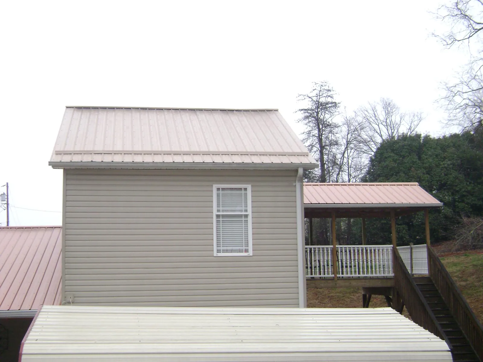 Tan metal roofs on a two story addition and attached porch, from a Roof Replacement job in Nottawa